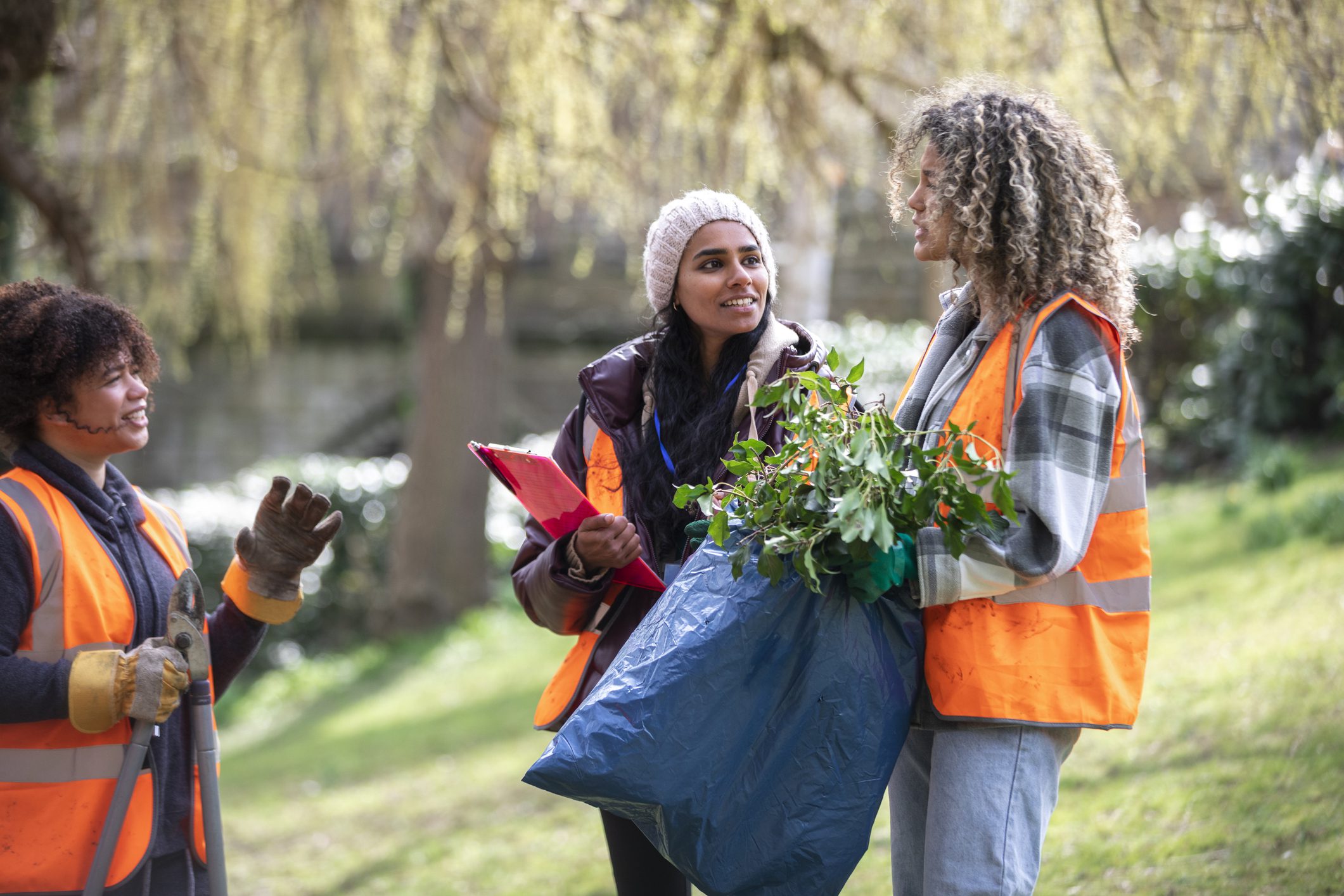 Two volunteers collecting trash outdoors near a pond.
