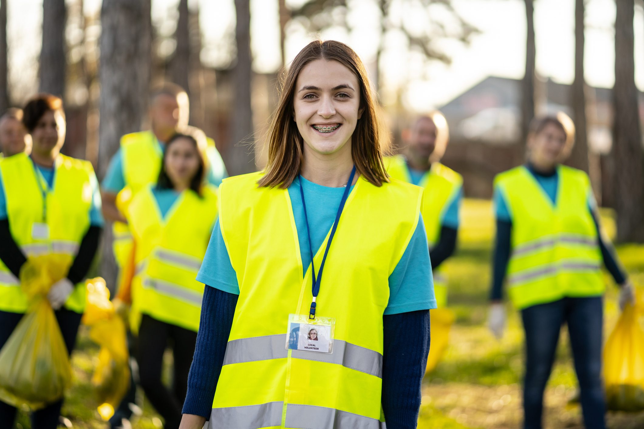Young woman in a yellow safety vest smiling outdoors with a group.