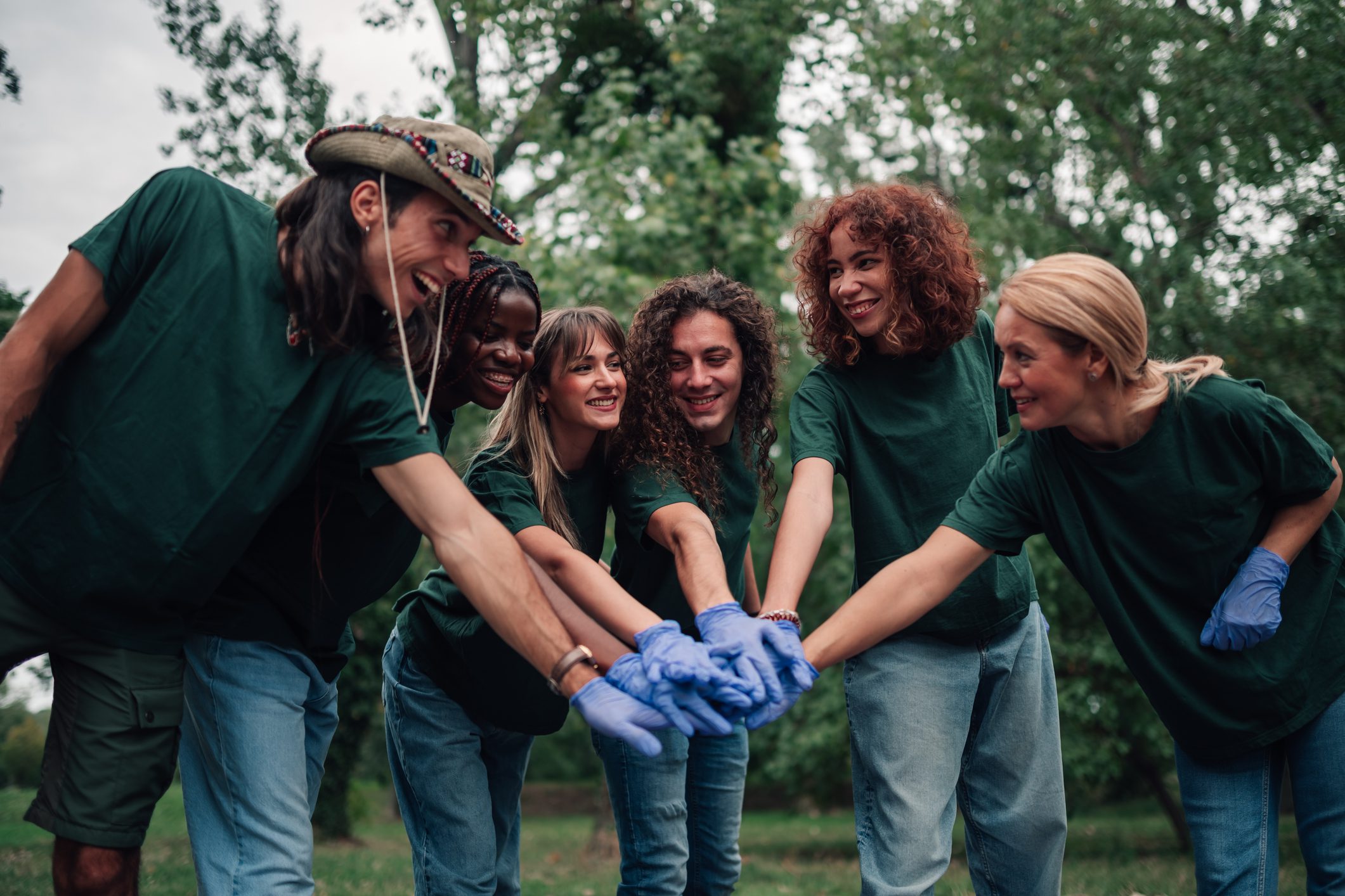 A group of friends wearing green shirts join hands outdoors showing unity.