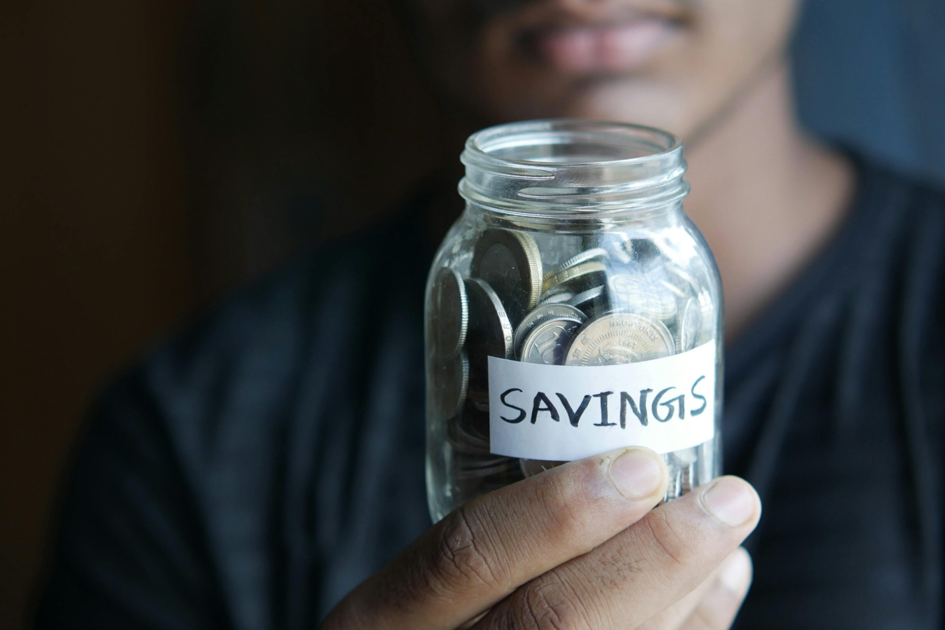 Person holding a jar labeled 'SAVINGS' filled with coins.