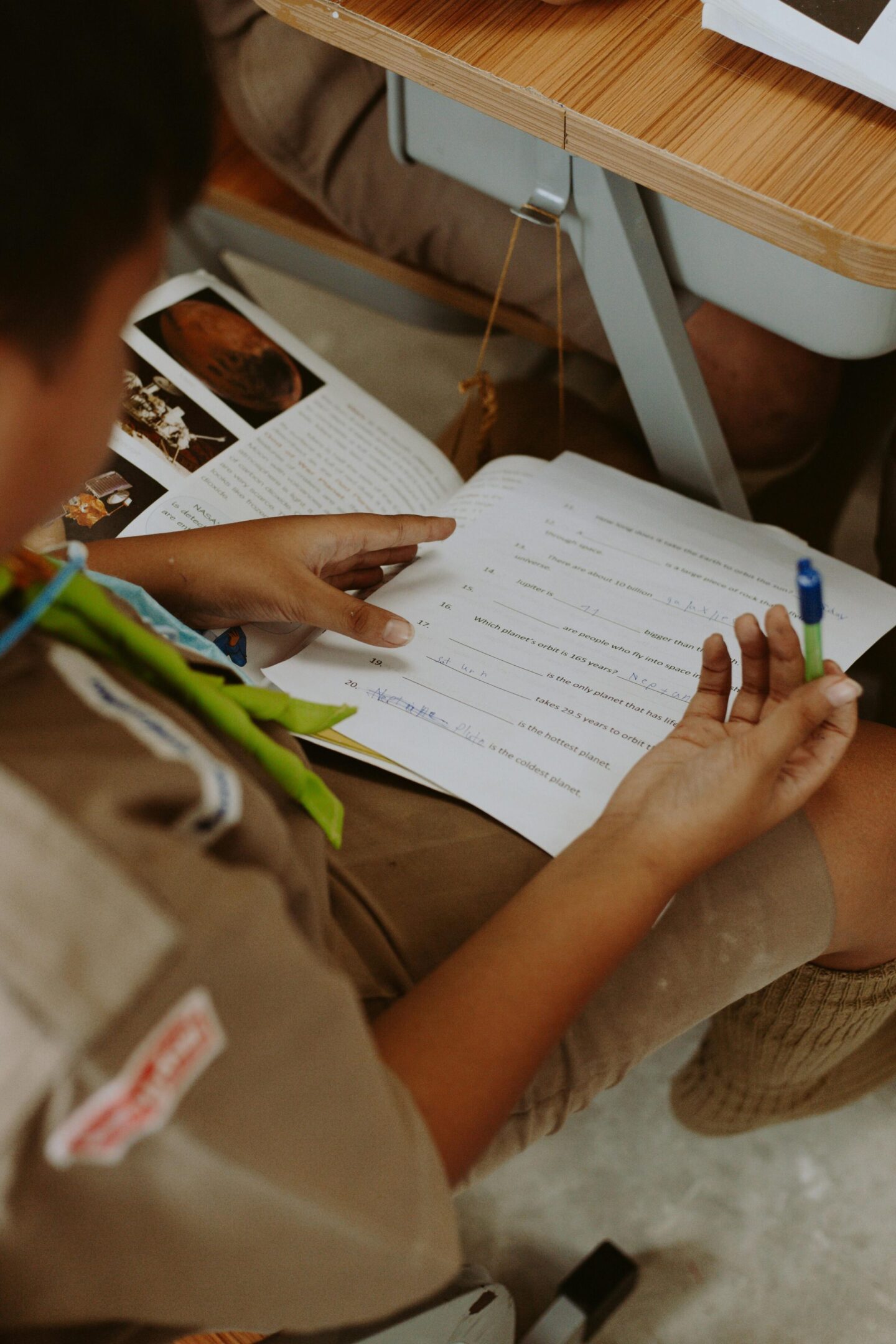 A child in scout uniform writing on a paper with a pen.