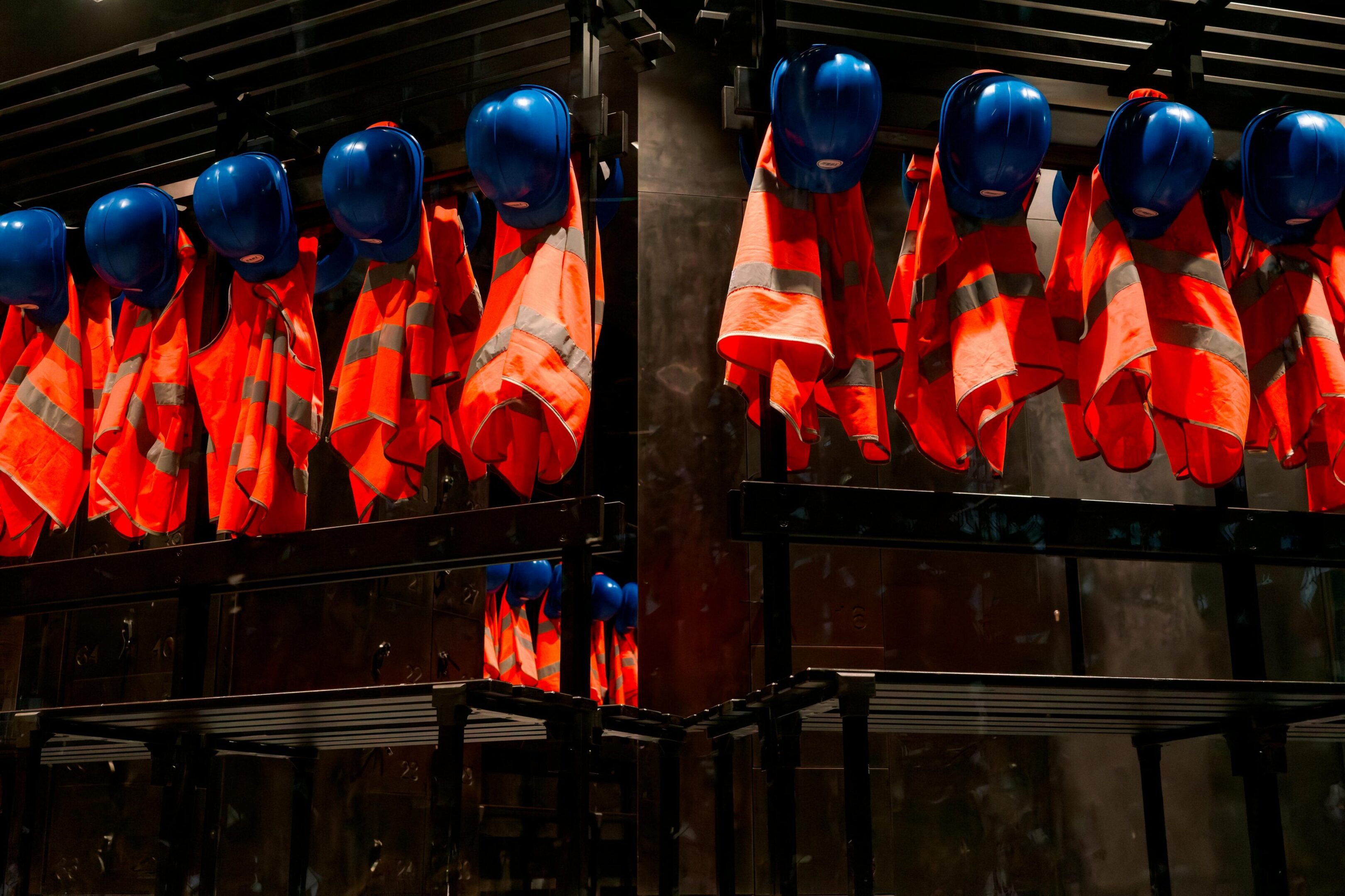 Blue helmets and orange safety vests hanging on hooks in a dimly lit industrial setting.