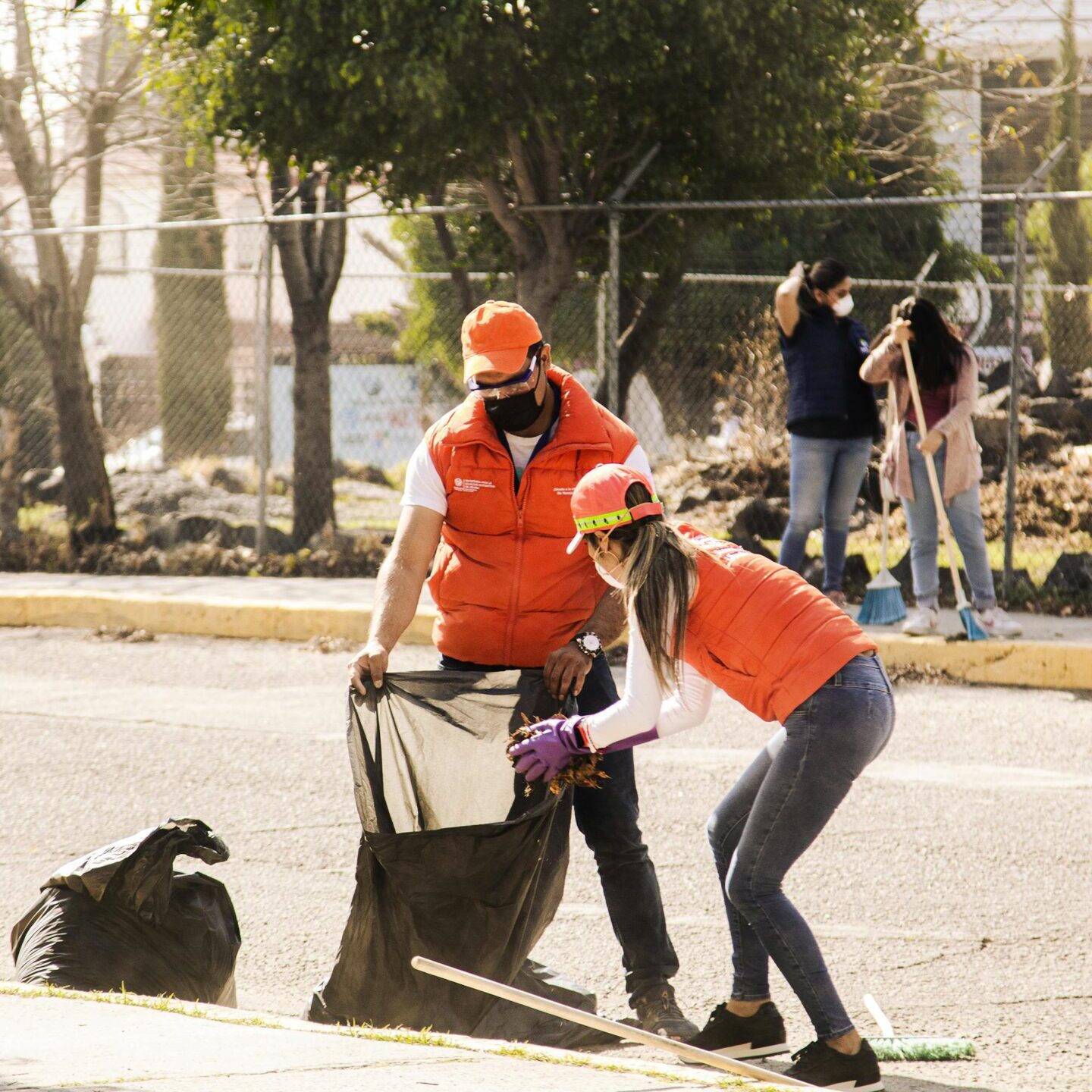 Two volunteers cleaning a park area with trash bags.
